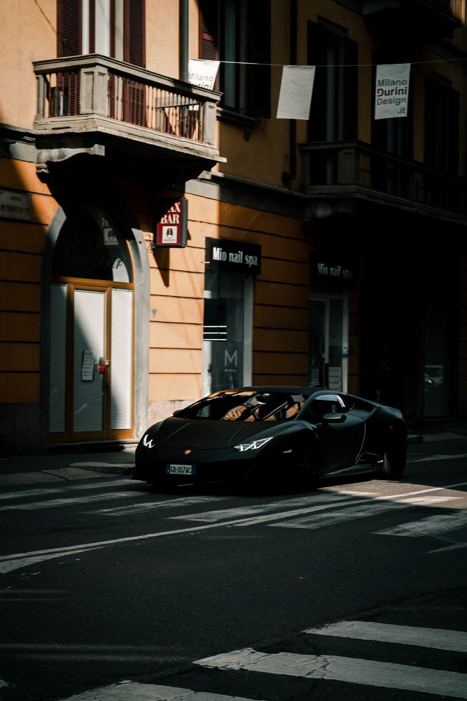 A dark Lamborghini parked along a sunlit city street